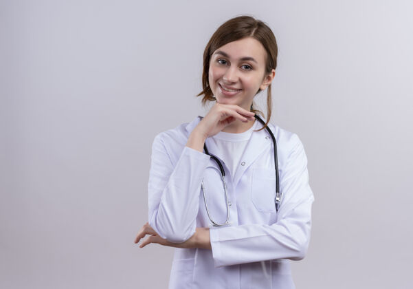 女人面带微笑的年轻女医生穿着医用长袍 手持听诊器 将手放在下巴下面的隔离白墙上 留有复印空间听诊器手年轻人