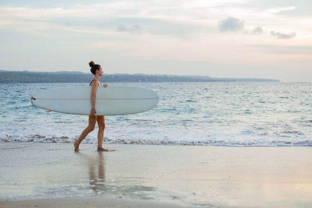 女孩美丽的女孩拿着冲浪板站在沙滩上海洋热带冲浪
