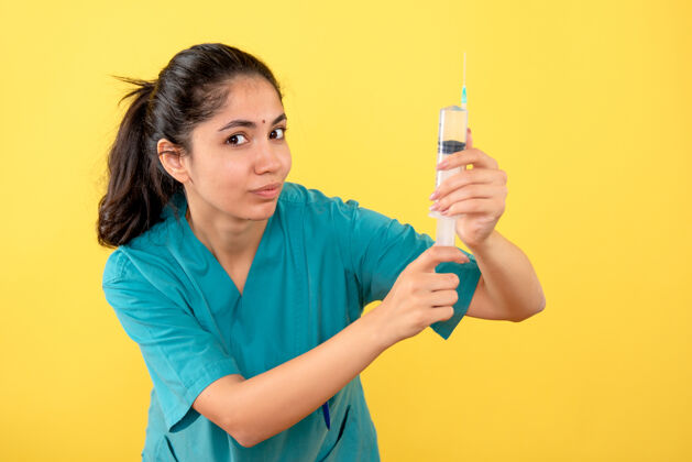 工作站在黄色墙上的年轻女医生拿着注射器的正视图工作肖像站