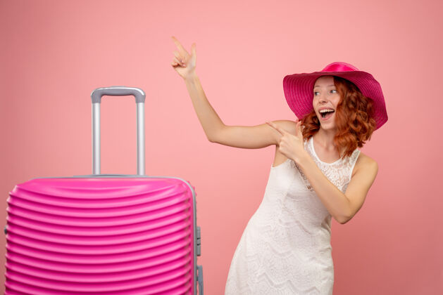 航行年轻的女性游客与粉红色的帽子和粉红色的墙壁上的包的正面视图假期情感前面