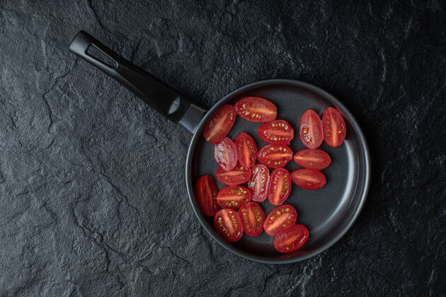 美味在黑底黑煎锅上切半个新鲜的樱桃番茄叶子切割切片