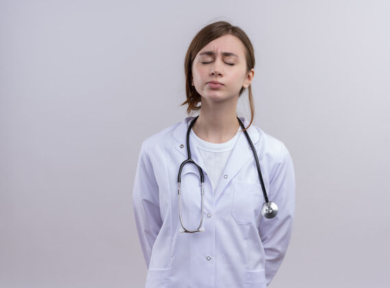 长袍疲惫的年轻女医生穿着医用长袍和听诊器 闭着眼睛站在隔离的白墙上 留着复印空间听诊器年轻女