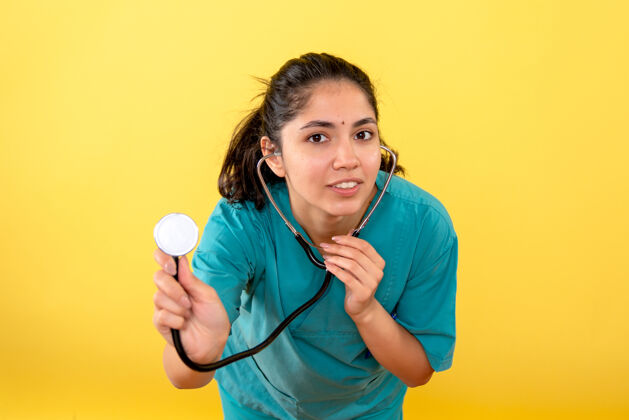 护理黄色墙上带听诊器的年轻女医生的正面图人医院听诊器