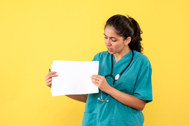 快乐黄色墙上站着一位穿着制服 拿着文件的漂亮女医生的正视图信心站纸