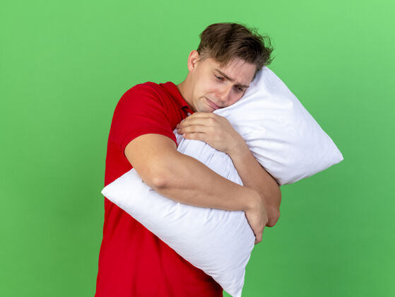 躺下悲伤的年轻英俊的金发病夫抱着枕头在绿色的背景上孤独地往下看悲伤年轻疾病