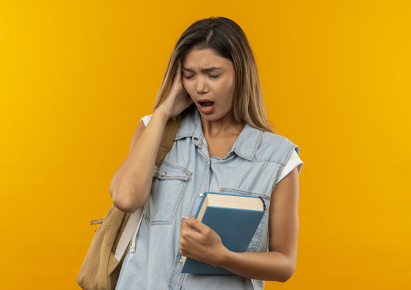 头疼痛的年轻漂亮的学生女孩戴着背袋拿着书把手放在头上头痛闭着眼睛孤立在橙色的复印空间女孩复制封闭