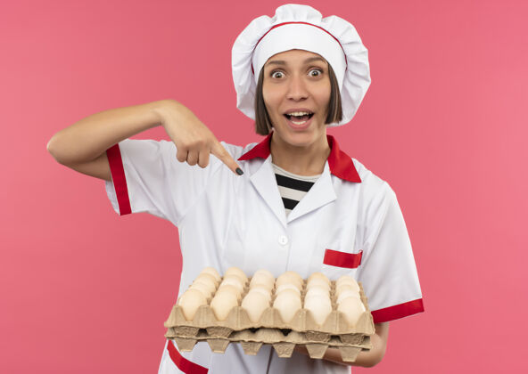 年轻穿着厨师制服的年轻女厨师手拿并指着一盒粉红色的鸡蛋指向印象纸箱