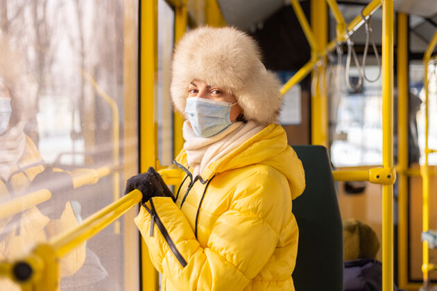车站一个穿着暖和衣服的年轻女子在一个冬天的城市公共汽车上的明亮的阳光肖像时尚检疫防护面罩