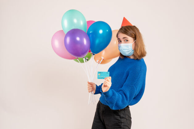 乐趣戴着面具拿着五颜六色气球的年轻女子 白色的银行卡气球生日吹