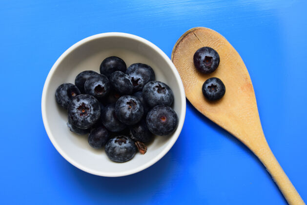 饮食高角度拍摄一个白色碗蓝莓附近的木勺隔离在一个蓝色的墙壁素食早餐金属