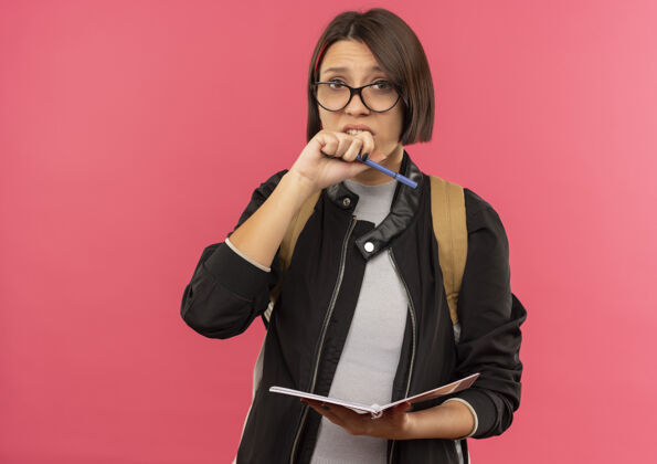 焦虑焦急的年轻女学生戴着眼镜 背着书包 拿着笔记本和笔 手放在离嘴很近的地方 用粉色隔开 留着复印空间嘴笔记包
