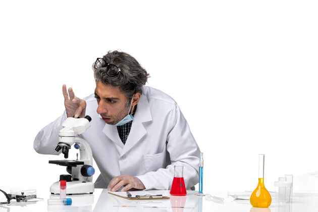 正面穿着白色医疗服的中年科学家使用显微镜的正视图显微镜实验室技师