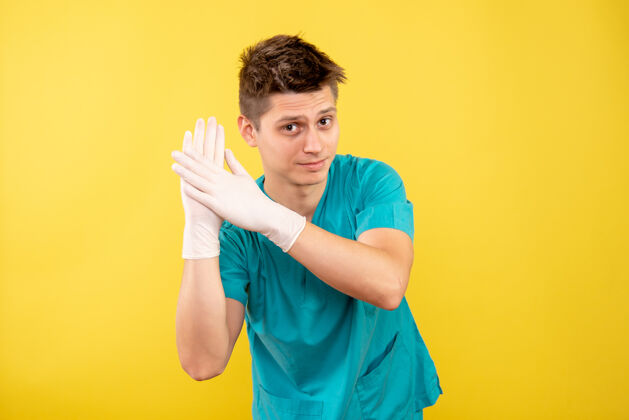 穿着正面图年轻的男医生穿着医疗服 戴着黄色背景的手套卫生休闲年轻男性医生