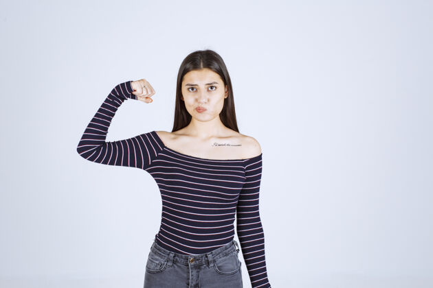 女性穿着条纹衬衫的年轻女子展示她的手臂肌肉和拳头年轻成人力量