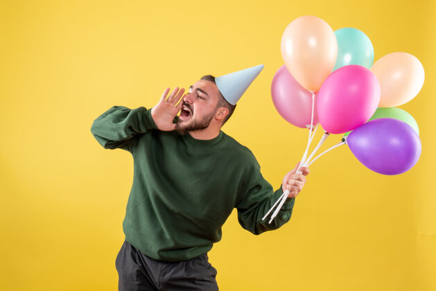 聚会正面图黄色背景上手持彩色气球的年轻男性生日人气球