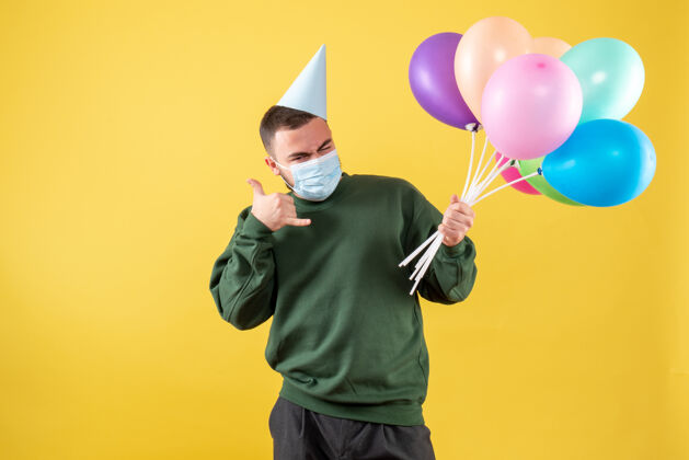 生日正面图黄色背景上手持彩色气球的年轻男性快乐聚会乐趣