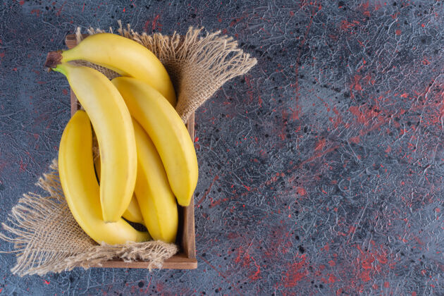 健康一堆新鲜的香蕉放在木箱里 放在五颜六色的表面上新鲜簇生
