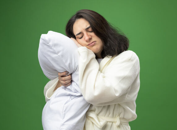 长袍皱眉的年轻白种人病女孩穿着长袍站在侧视图拥抱枕头把它的头孤立在绿色背景拥抱女孩站立