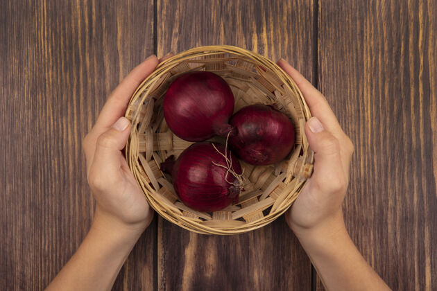 食物顶视图：女性手拿着一碗健康的红洋葱放在木墙上新鲜的木头餐