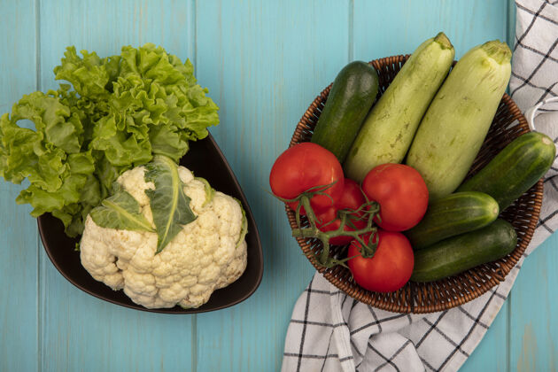 营养新鲜蔬菜的俯视图 如西红柿 黄瓜和西葫芦放在格子布上的桶上 菜花和莴苣放在蓝色木墙上的碗上生菜农场花椰菜