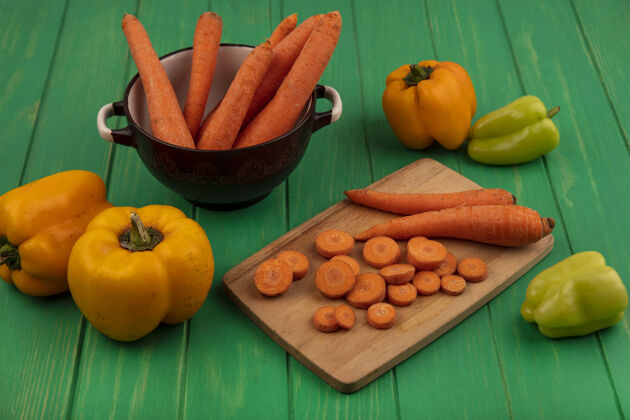 食物顶视图的根蔬菜胡萝卜在一个碗切碎片在一个木制的厨房板与甜椒隔离在一个绿色的木墙上蔬菜膳食根