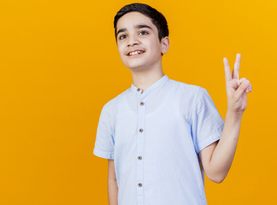 男孩微笑的年轻白人男孩在一旁做和平标志孤立的橙色背景与复制空间侧线橙色年轻