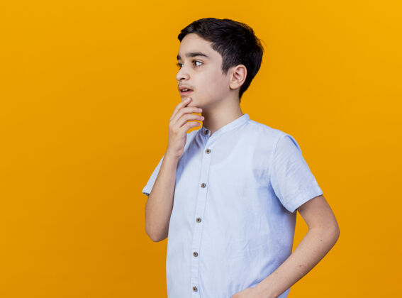橙色印象深刻的年轻白人男孩站在侧视图触摸下巴看起来直孤立的橙色背景与复制空间查看个人资料下巴