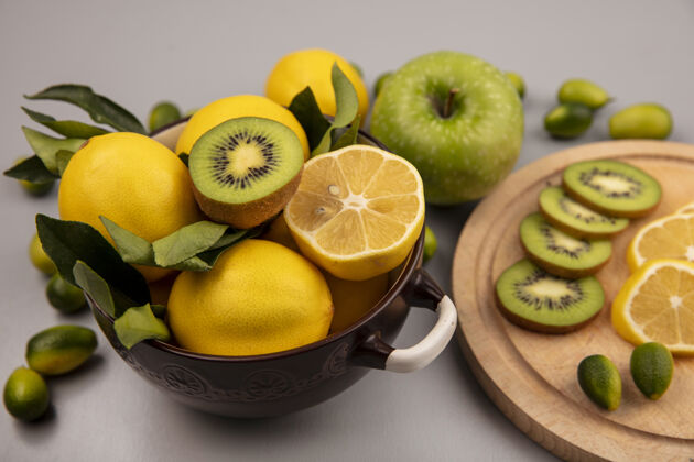 切片顶视图：柠檬放在碗里 猕猴桃和柠檬片放在木制的厨房板上 金盏花和苹果被隔离在白色的墙上配料水果新鲜