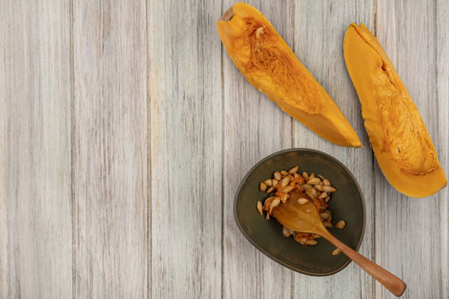 庆祝顶视图新鲜的橙色南瓜片与种子在一个碗与木勺在一个灰色的木制墙壁与复制空间季节木头新鲜