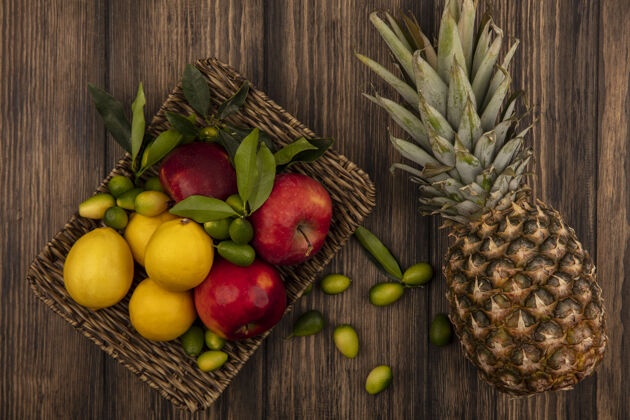 人新鲜水果的俯视图 如柳条托盘上的苹果 柠檬和金盏花 菠萝被隔离在木墙上苹果农业菠萝