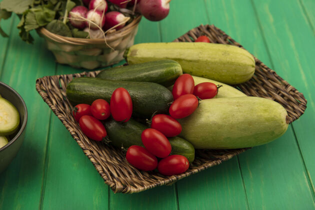 新鲜顶视图蔬菜 如李子 西红柿 黄瓜和西葫芦在柳条托盘与萝卜在一个绿色的木桶墙壁桶黄瓜李子