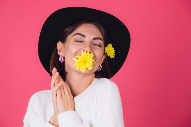 无忧无虑时尚的女人戴着帽子 微笑着两个黄色的紫苑 可爱的捧着一朵花在口中春意盎然 快乐的情感与世隔绝的空间节日庆祝成人
