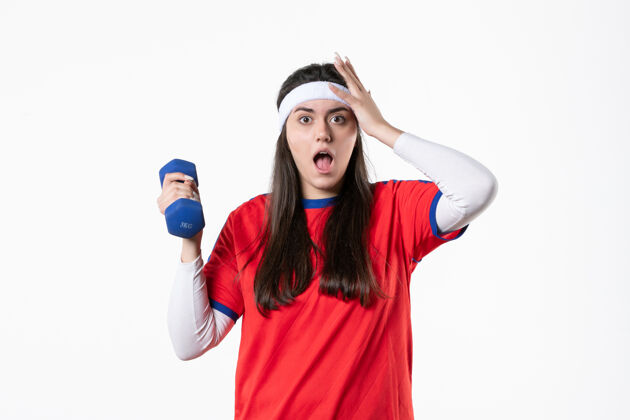 哑铃正面图穿着运动服的年轻女性在白墙上用哑铃锻炼视图锻炼人