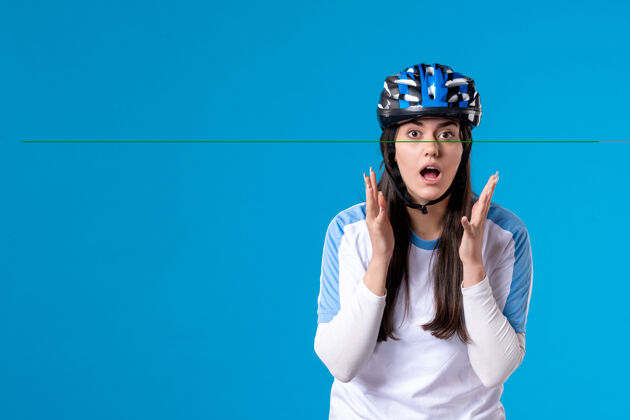 运动前视图穿着运动服的年轻女性 蓝色墙上戴着头盔水平惊喜自行车