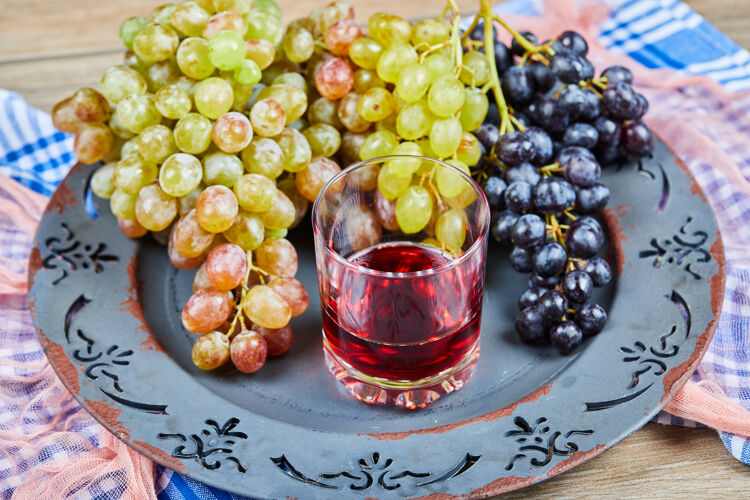 特写一堆葡萄和一杯果汁放在陶瓷盘子里 还有桌布食物餐桌水果