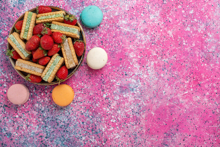 美味美味的华夫饼干的顶视图 粉色表面有新鲜的红色草莓和法国马卡龙草莓新鲜饼干