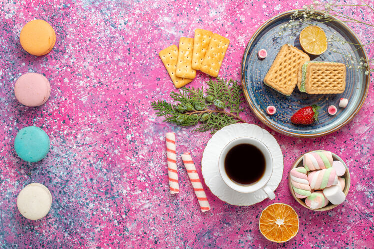麦卡龙粉红色表面上有一杯茶和麦卡龙的甜华夫饼俯视图咖啡早餐含糖