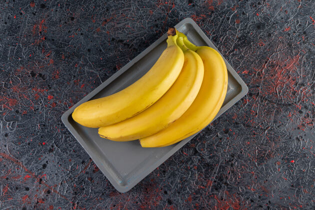 营养把一束多汁的黄色香蕉放在深色盘子里水果美味香蕉