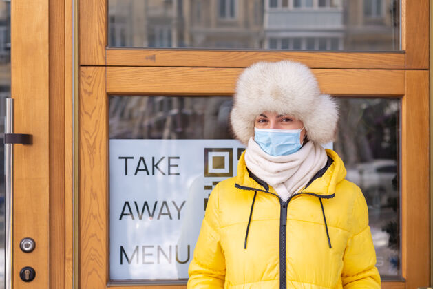口罩在寒冷的冬日 快乐的年轻女子在餐厅门口 刻字 吃外卖开放餐厅企业家
