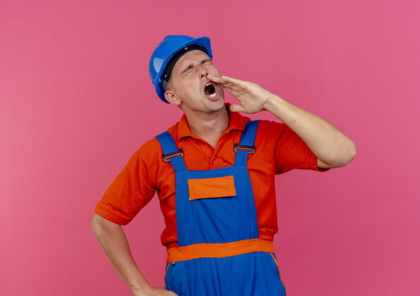 建筑工人年轻的男建筑工人闭着眼睛 穿着制服 戴着安全帽 叫着粉红色的人闭嘴男性年轻
