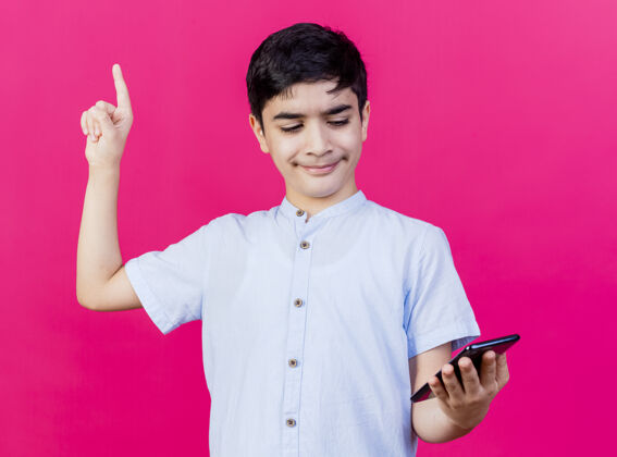 年轻人印象深刻的小男孩拿着手机看着粉红色的墙上孤立的指向上人拿着指着