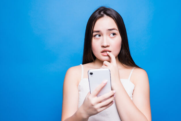 青少年悲伤忧郁的亚洲女人用智能手机孤立在蓝色的墙上抑郁症年轻美丽