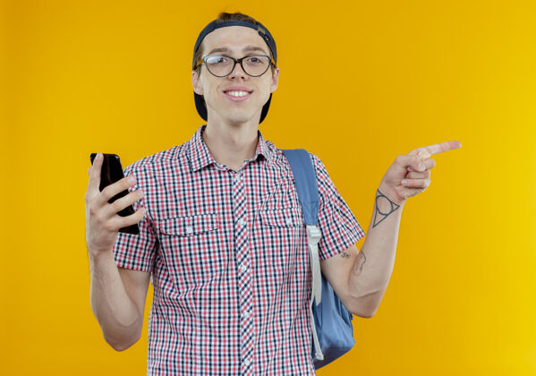 背部带着微笑的年轻学生男孩背着书包 戴着眼镜和帽子 手里拿着电话 指着旁边的白色年轻男孩背景