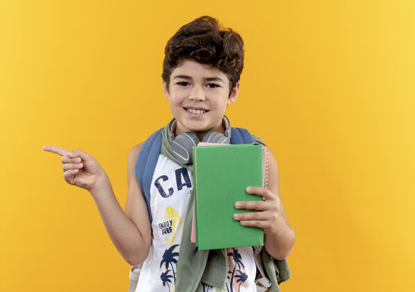 壁板面带微笑的小男生背着书包 戴着耳机 手里拿着书 指着隔离在黄色边上的复印空间空间男孩背