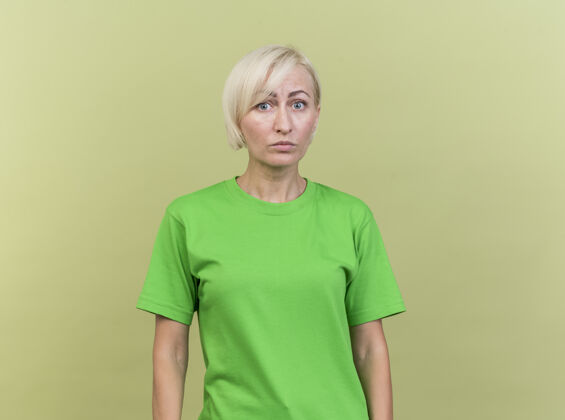 感情令人印象深刻的中年金发女子看着前面孤立的橄榄绿墙上人衣服金发