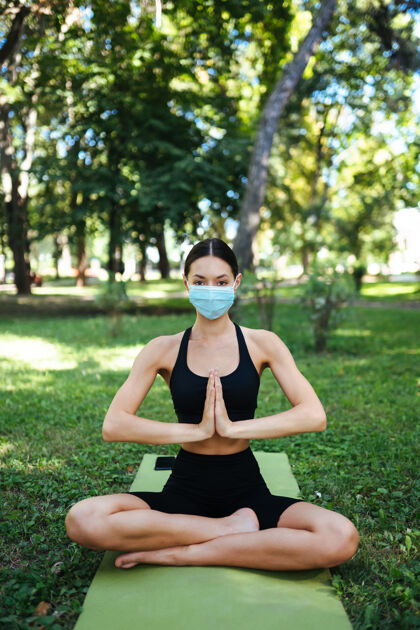 训练戴着医用防护面具的运动型年轻女子 早上在公园里做瑜伽面具运动放松