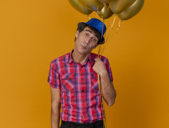 印象印象深刻的中年党人戴着党的帽子拿着气球看着前面孤立的橙色墙壁气球人衣服