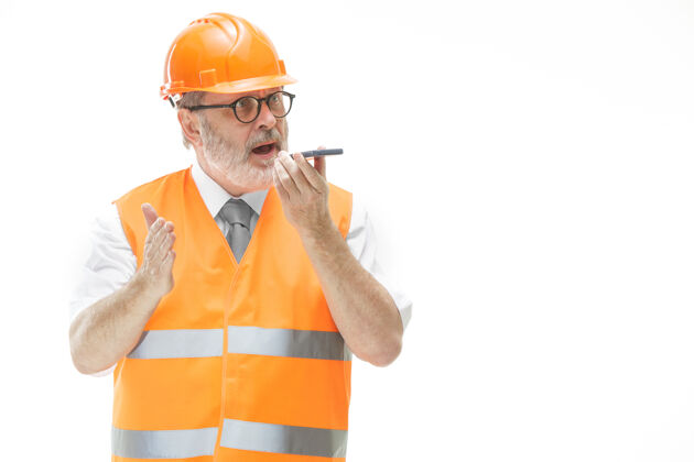 现场一个穿着建筑背心 戴着橙色头盔的建筑工人正在用手机谈论一些事情男性工人业务