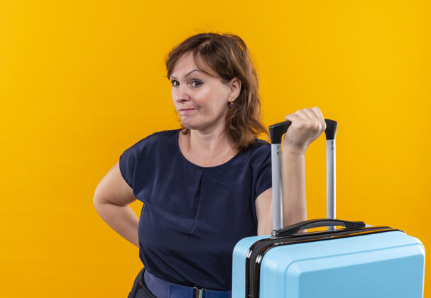 女人望着旁边一个中年旅行家妇女提着手提箱孤零零地站在黄色的墙上手提箱壁板中年