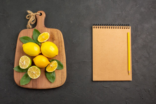 笔记本在深灰色的桌子上俯瞰新鲜柠檬酸水果柑橘酸橙水果黄色酸橙新鲜柠檬